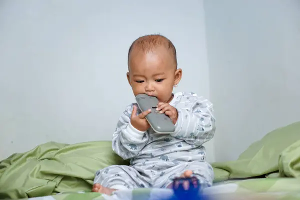 1 yaşın altındaki küçük Asyalı kız uyanmış ve uzaktan kumandayla oynuyordu..