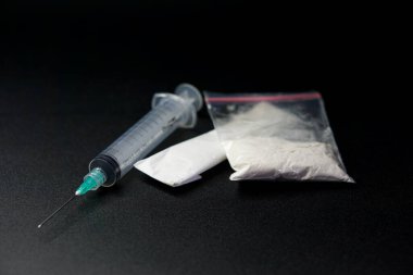 Plastiğe sarılı metamfetamin tipi uyuşturucular ve siyah arka planlı bir şırınga.