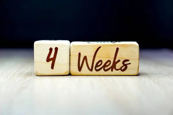 Siyah arka planı olan tahta bir küpte 4 haftalık hamilelik yaşı dönüm noktası.