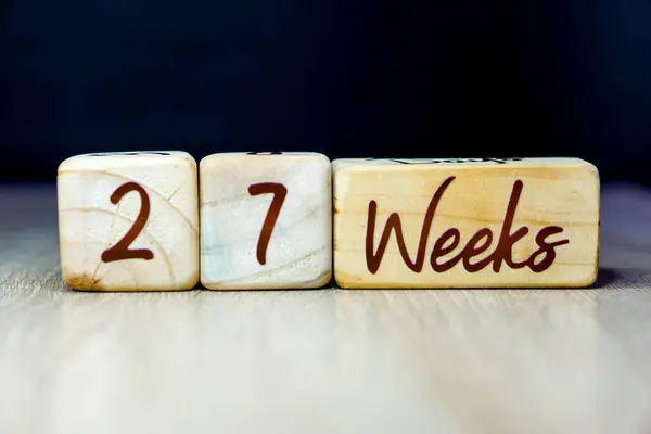 27 week pregnancy age milestone written on a wooden cube with a black background