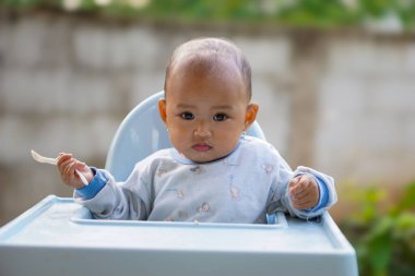 Bebek beslenme koltuğunda otururken yemek yiyen sevimli ve sevimli Asyalı bir kızın portresi.