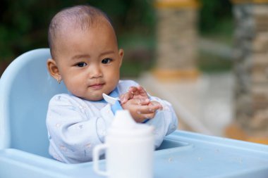Bebek beslenme koltuğunda otururken yemek yiyen sevimli ve sevimli Asyalı bir kızın portresi.