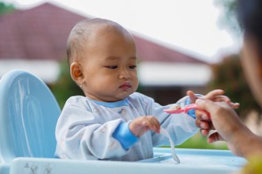 Bebek beslenme koltuğunda otururken yemek yiyen sevimli ve sevimli Asyalı bir kızın portresi.