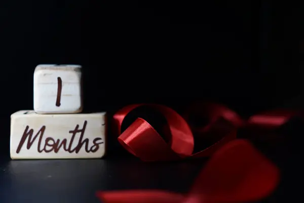 Bebeğin yaşının dönüm noktası siyah arka planda kırmızı kurdeleli tahta bir küpte yazılı.