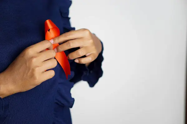 Aralık ayındaki Dünya AIDS Günü için göğsünde kırmızı kurdele tutan Asyalı bir kadının portresi. Sağlık hizmetleri kavramı