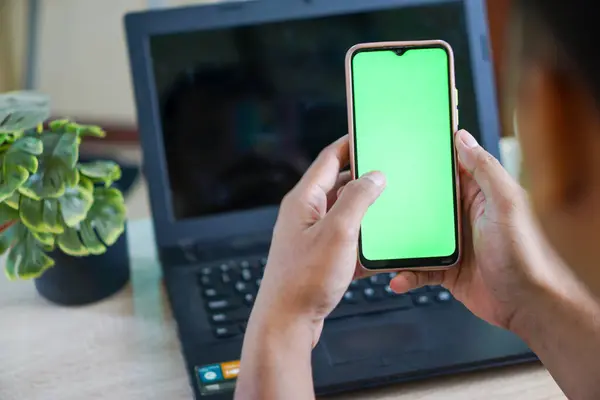 Yakından çekilmiş bir fotoğraf. Elinde boş yeşil ekranlı bir cep telefonu olan bir adam.