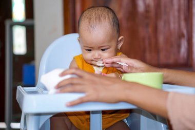 Bebek beslenme koltuğunda otururken yemek yiyen sevimli ve sevimli Asyalı bir kızın portresi.