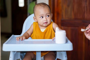 Bebek beslenme koltuğunda otururken yemek yiyen sevimli ve sevimli Asyalı bir kızın portresi.
