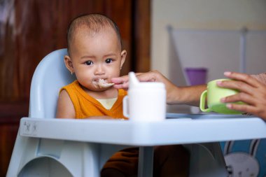 Bebek beslenme koltuğunda otururken yemek yiyen sevimli ve sevimli Asyalı bir kızın portresi.