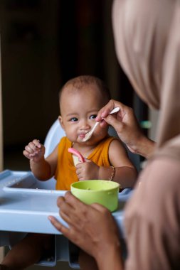 Bebek beslenme koltuğunda otururken yemek yiyen sevimli ve sevimli Asyalı bir kızın portresi.