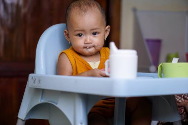 Bebek beslenme koltuğunda otururken yemek yiyen sevimli ve sevimli Asyalı bir kızın portresi.