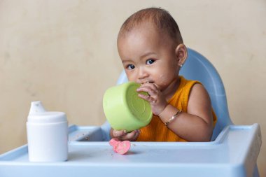 Bebek beslenme koltuğunda otururken yemek yiyen sevimli ve sevimli Asyalı bir kızın portresi.