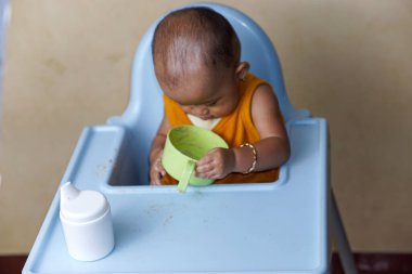 Bebek beslenme koltuğunda otururken yemek yiyen sevimli ve sevimli Asyalı bir kızın portresi.