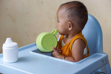 Bebek beslenme koltuğunda otururken yemek yiyen sevimli ve sevimli Asyalı bir kızın portresi.