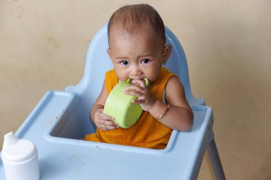 Bebek beslenme koltuğunda otururken yemek yiyen sevimli ve sevimli Asyalı bir kızın portresi.