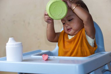Bebek beslenme koltuğunda otururken yemek yiyen sevimli ve sevimli Asyalı bir kızın portresi.