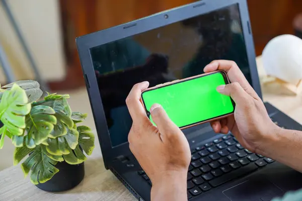 Yakından çekilmiş bir fotoğraf. Elinde boş yeşil ekranlı bir cep telefonu olan bir adam.