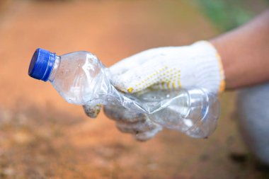 Plastik şişe atıklarını toplayan beyaz eldivenli bir adamın eli.