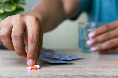 Bir adamın eli, sağlık kavramları için bir bardak su tutarken bir masanın üzerinde ilaç topluyor.