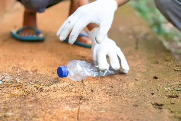 Plastik şişe atıklarını toplayan beyaz eldivenli bir adamın eli.