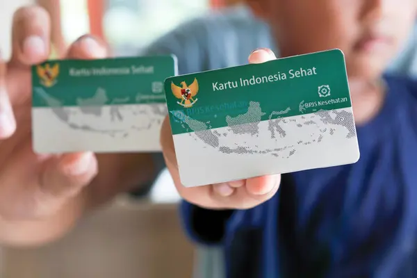 Subang, Batı Java - Endonezya, 24 Şubat 2024: Endonezya Sağlık Kartı (Endonezya Hükümeti Sağlık Kartı), KIS kartı veya BPJS kartı tutan ve gösteren bir çocuk ve ailesi