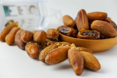 Ahşap bir kapta servis edilen kurutulmuş hurmaların yakın plan fotoğrafı ve beyaz arka planda izole edilmiş beyaz fener.