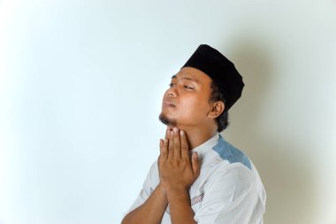 Müslüman kıyafetleri içinde Asyalı bir Müslüman, Ramazan ayında beyaz bir arkaplanda oruç tutarken susuzluk çekiyor..