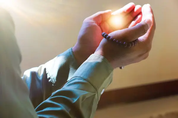 Elleri Müslümanların ellerinde dua boncukları tutan, avuçlarında ışık tutan bir adamın elleri.