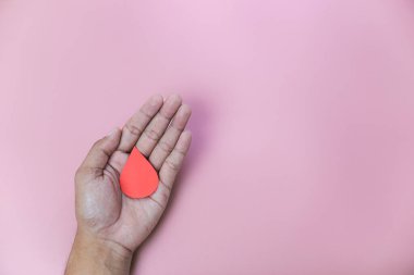 Bir adamın eli bir damla donör kanı tutuyor. Pembe arka plan izole edilmiş. Dünya kan bağışı günü konsepti, sağlık sigortası, akıl sağlığı günü. Boşluğu kopyala