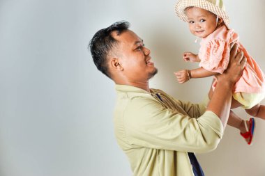 Sevimli bebeğini sevimli bir şapkanın içinde tutan mutlu bir baba. İkisi de sıcak bir şekilde gülümsüyor, sevgi dolu bir aile anı sergiliyorlar..