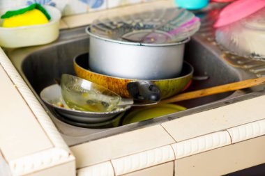 Kirli bulaşık, tencere ve çatal bıçak dolu bir lavabo, yemekten sonra tipik bir ev ortamını gösteriyor, temizlik ve yıkama ihtiyacını vurguluyor..