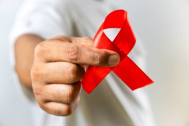 AlDS farkındalığını ve HIV 'in önlenmesine verilen desteği sembolize eden kırmızı kurdeleyi tutan bir el resmi, beyaz bir arkaplanda izole edilmiş..
