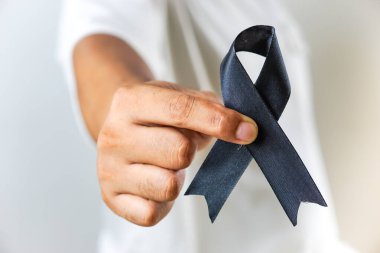 Elinde siyah farkındalık kurdelesi olan bir kişi yas tutmayı, hatırlamayı ya da bir amaç için farkındalığı sembolize eder. Kurdele açık renkli bir arkaplanda tutuluyor..
