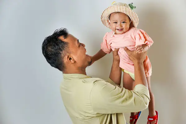 stock image A happy father holding his adorable baby daughter in a cute hat. They are both smiling warmly, showcasing a loving family moment.