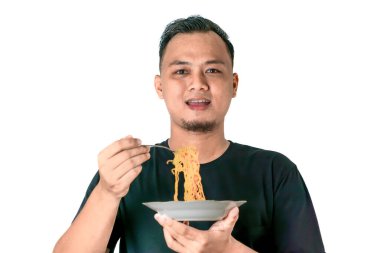 A man wearing a black shirt is holding a plate of noodles and eating with a fork. He looks content and is posing against a white background clipart