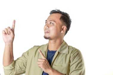 Bej ceketli bir adam iki eliyle yukarıyı gösterir, gülümserken, aynı yöne bakarken, düz bir arkaplana bakar..