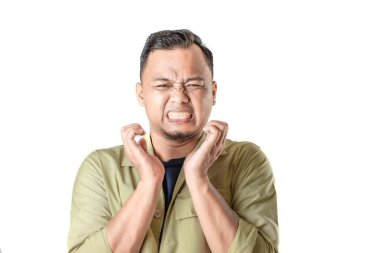 Bej ceketli bir adam endişeli ve tedirgin bir ifade sergiler, dişlerini sıkar ve ellerini yüzüne yakın tutar..