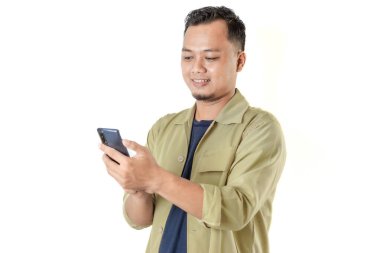 Açık bej ceketli bir adam gülümsüyor ve akıllı telefonuna bakıyor. Arka plan sade ve iyi aydınlatılmış..