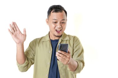 Bir adam, mavi bir gömlek üzerine bej bir ceket giymiş, beyaz bir arka fona karşı duran akıllı telefon ekranına bakarken sevinçle el sallıyor..