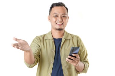 Bej ceketli gülümseyen bir adam bir elinde akıllı bir telefon, diğerinde ise bir şeyi açıklamaya ya da birine hoş geldin der gibi el kol hareketi yapar..