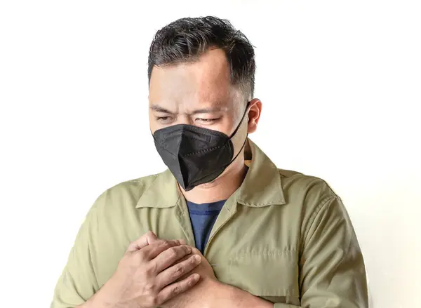 stock image A person wearing a black mask and light beige jacket crosses his arms over his chest, potentially indicating heart pain or a heart attack.