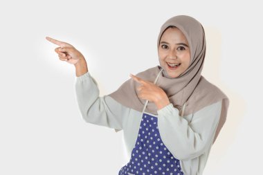 Başörtüsü ve önlük takan bir kadın akıllı bir telefon tutar, parmağını kaldırır, neşeli bir ifadeyle bir şeyi açıklar ya da gösterir gibi..