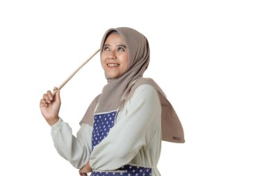 Başörtüsü ve önlük takan bir kadın akıllı bir telefon tutar, parmağını kaldırır, neşeli bir ifadeyle bir şeyi açıklar ya da gösterir gibi..