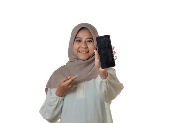 Başörtüsü takan bir kadın gülümsüyor ve elindeki akıllı telefonu göstererek gururla gösteriyor. Arkaplan beyaz ve sade.