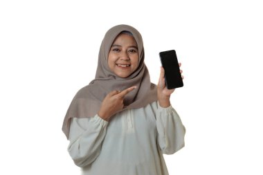 Başörtüsü takan bir kadın gülümsüyor ve elindeki akıllı telefonu göstererek gururla gösteriyor. Arkaplan beyaz ve sade.