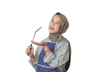 Başörtüsü ve önlük takan bir kadın akıllı bir telefon tutar, parmağını kaldırır, neşeli bir ifadeyle bir şeyi açıklar ya da gösterir gibi..