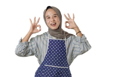 Başörtüsü ve önlük takan bir kadın akıllı bir telefon tutar, parmağını kaldırır, neşeli bir ifadeyle bir şeyi açıklar ya da gösterir gibi..