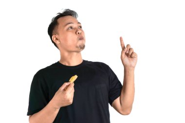 Siyah tişörtlü bir adam yukarı bakarken bir parça yiyecek tutar, düşüncelere dalmış. İfadesi, atıştırmalığının tadını çıkarırken önemli bir şey düşündüğünü gösteriyor..