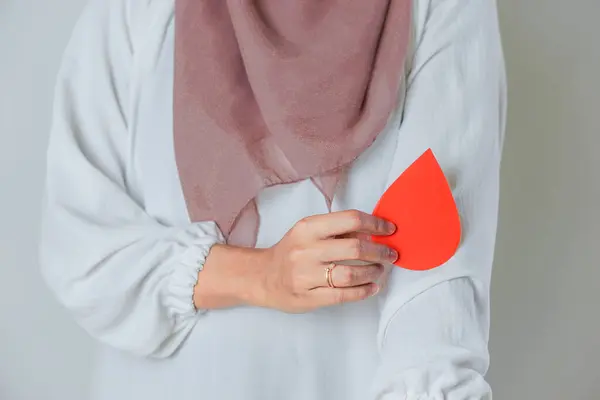 Açık renk bluz giyen ve elinde kan damlası şeklinde kırmızı bir kağıt tutan bir kadın kan bağışını simgeliyor. konsept kan bağışı günü