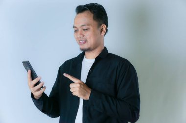 Siyah tişörtlü ve beyaz tişörtlü gülümseyen Asyalı bir adam elinde bir cep telefonu tutuyor ve onu işaret ediyor..